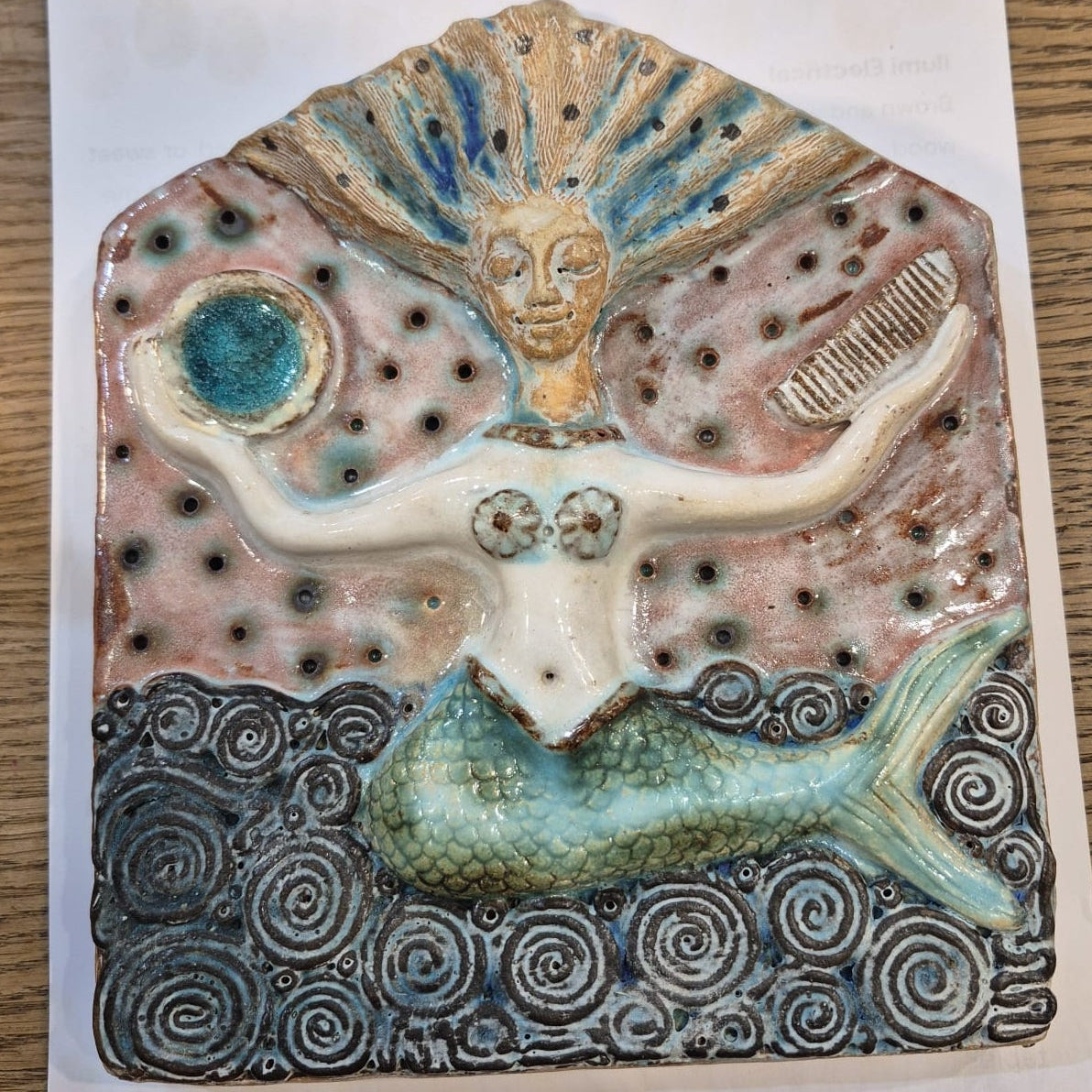 Ceramic artwork of a mermaid with shell-like head on a white background
